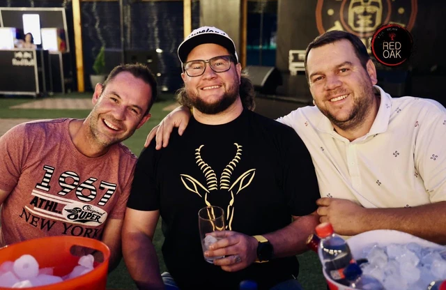 Three friends laughing together with drinks at the bar.
